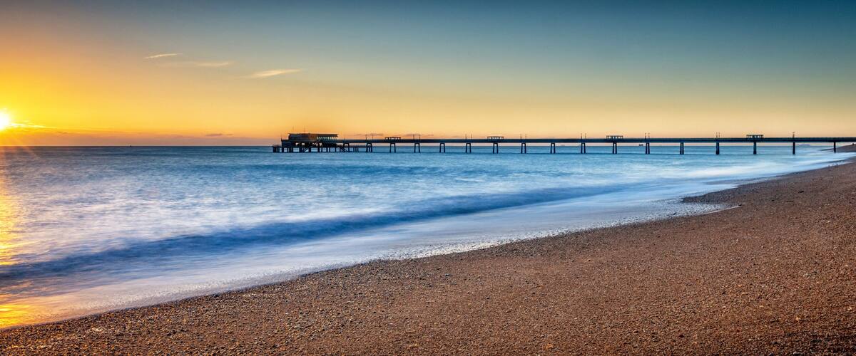 A beach with a pier extending into the ocean during sunset.