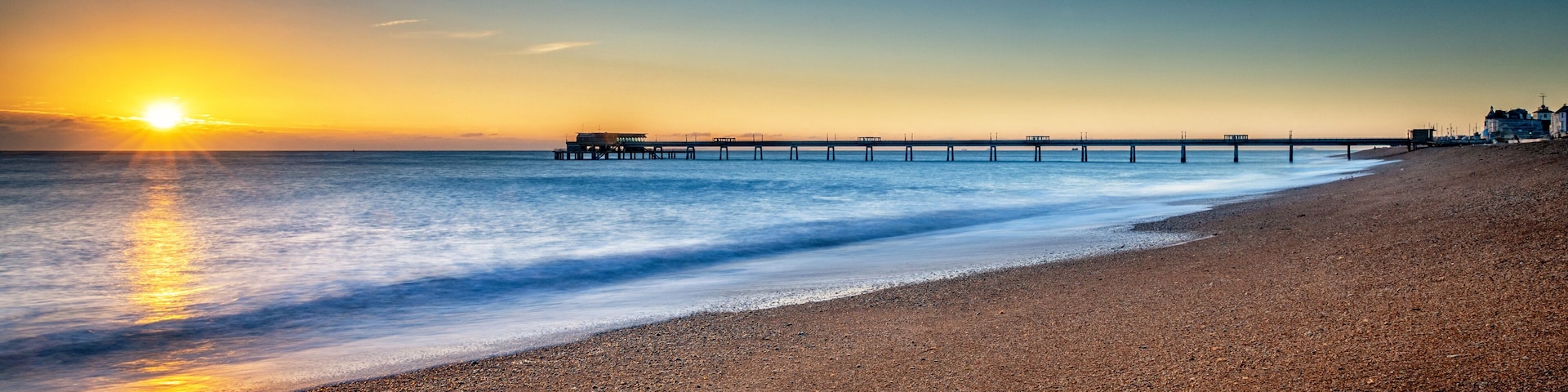 A beach with a pier extending into the ocean during sunset.