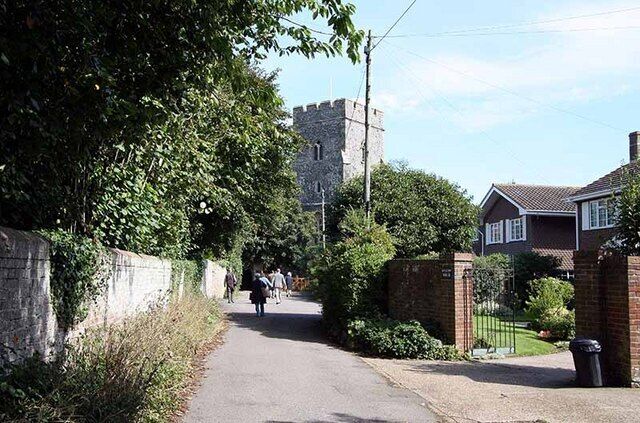 A narrow road flanked by houses and a stone tower in the distance.