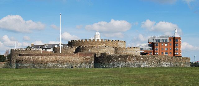 A historic fort with a central round tower, a flagpole, and a red brick building.