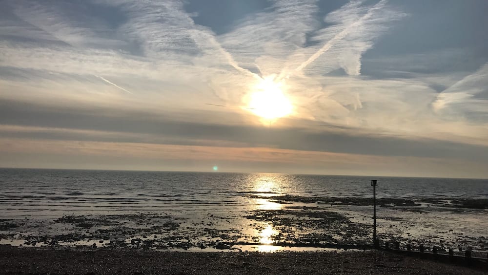 Ein Sonnenuntergang über einer felsigen Küstenlinie, die Sonne ist teilweise von Wolken verdeckt.