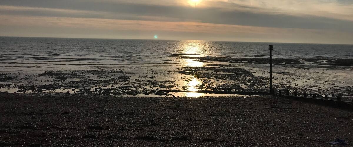 A sunset over a rocky shoreline with the sun partially obscured by clouds.