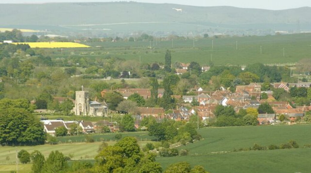 West Lavington from Strawberry Hill 452274 gives a view of West Lavington from a different direction. 'It lies far away from the coming and going of the great busy world,' wrote an inhabitant in 1875. Today, and for many decades, the great busy world speeds along the A360 from Salisbury to Devizes and threads its way precipitously through the chicane formed by the churchyard and the almshouses. In fact the main road spends about 8km in West Lavington parish, from the high downland south of Gore, the 'buried village of Salisbury Plain', past Gore Cross, where it is intersected by an important ridgeway, down a long descent beside landscaped woodland (known as The Warren) and into the pleasant valley where the village sits, then along some 2km of ribbon development associated with the linear village of Littleton Pannell, before leaving the parish north of the railway bridge. This journey is familiar to most Wiltshire travellers, and even without realising that chalk is giving way to Greensand and clay, many must feel as they pass along that here south Wiltshire ends and west Wiltshire begins" All this and more in: http://www.wiltshire.gov.uk/community/getconcise.php?id=237