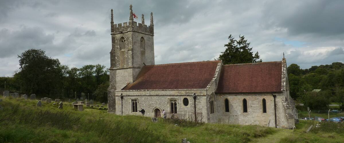 A historic church with a tall tower and a red-tiled roof, surrounded by a cemetery and lush greenery.