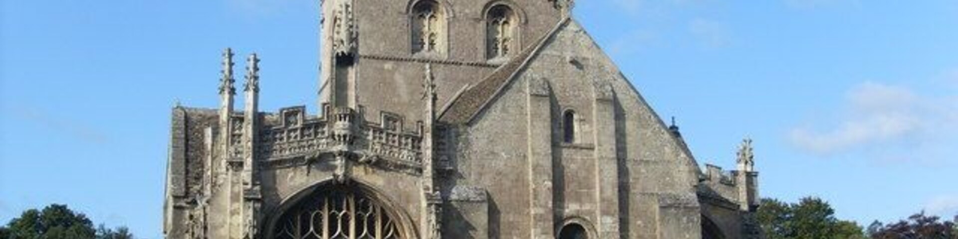 Eine historische Kirche mit hohem Turm, großen Bogenfenstern und einer steinernen Fassade.