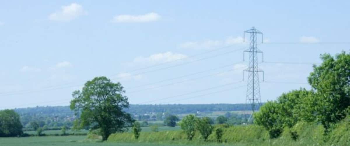A rural landscape with a green field, a dirt path, trees, and a distant power line tower.