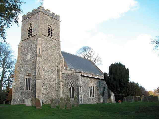 A stone church with a tall tower and a large tree in front.