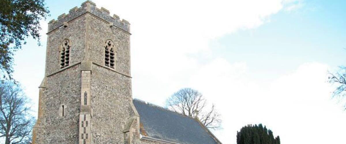 A stone church with a tall tower and a large tree in front.