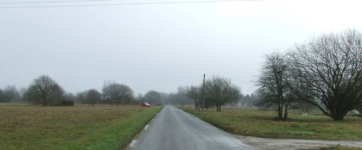 A rural road with a red car parked on the side.