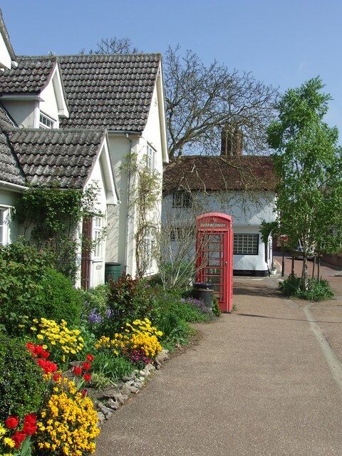 A quaint village with a red telephone booth, white houses, and a flower garden.