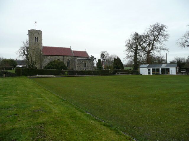 A church with a tower, a green field, and a small white building.
