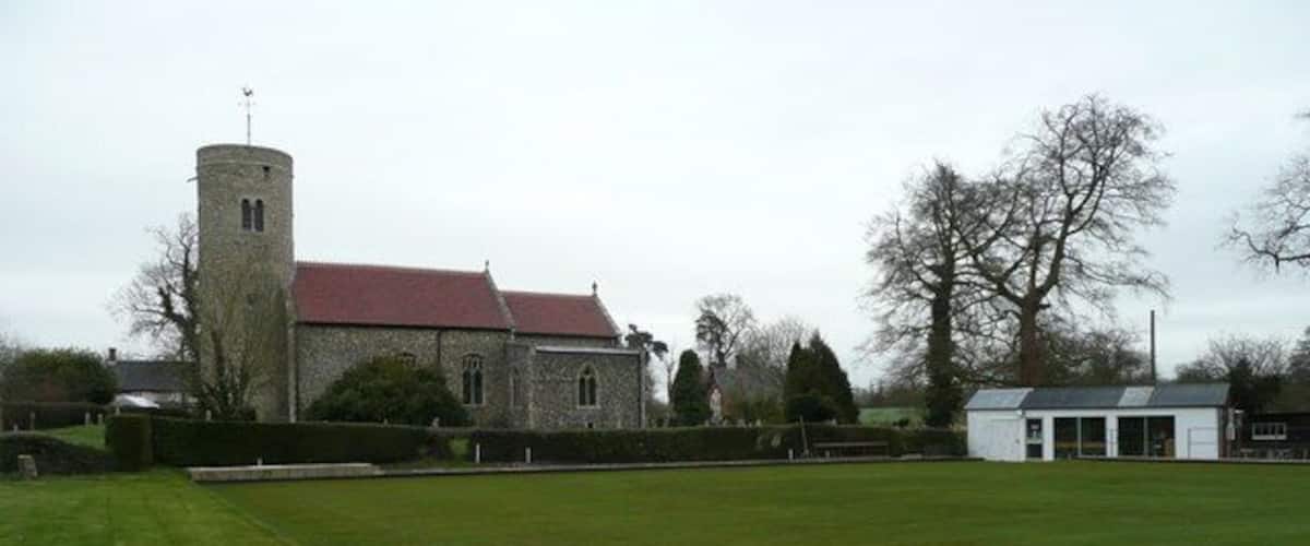 A church with a tower, a green field, and a small white building.