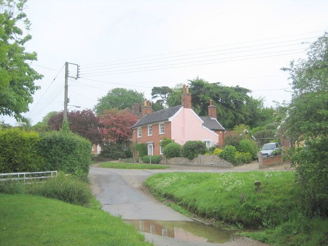 A rural road with a pink house, greenery, and a parked car.