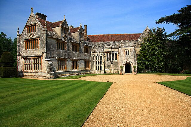 A large stone manor with a gravel driveway and well-manicured lawns.