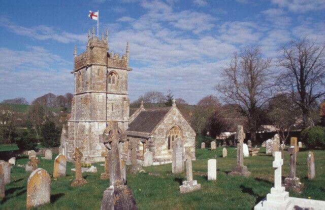 A church with a tall tower and a smaller building, surrounded by gravestones in a cemetery.