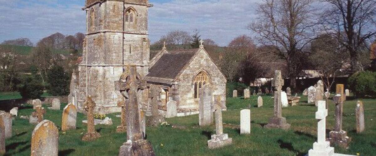 A church with a tall tower and a smaller building, surrounded by gravestones in a cemetery.