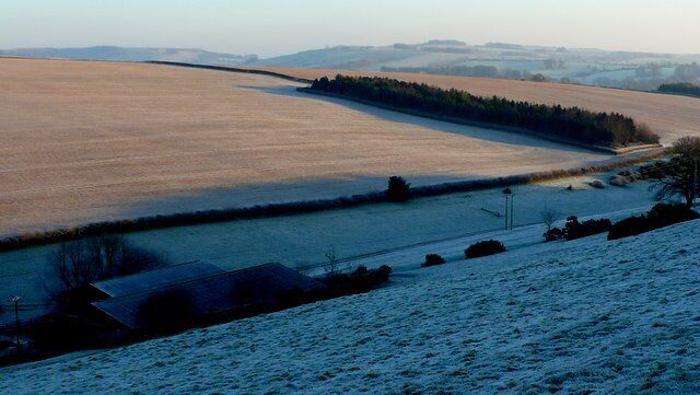 A snow-covered landscape with a frozen field, a small building, and distant hills.