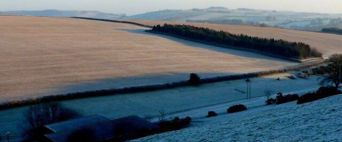 A snow-covered landscape with a frozen field, a small building, and distant hills.