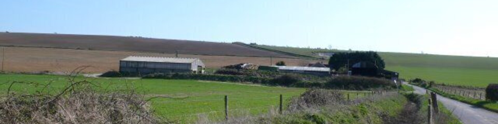 A rural landscape with a narrow road, green fields, and farm buildings.