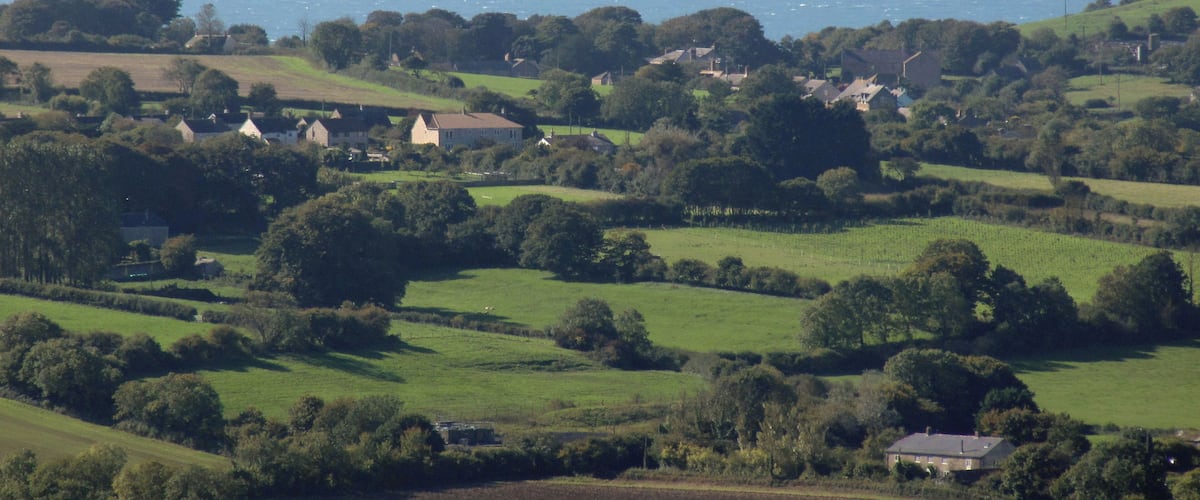 A coastal landscape with rolling hills, scattered houses, and a view of the sea.
