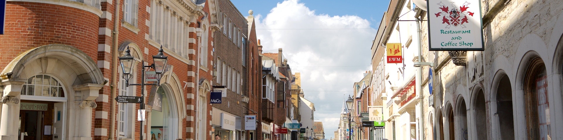 A bustling street with historic buildings, a clock tower, and various shops and cafes.
