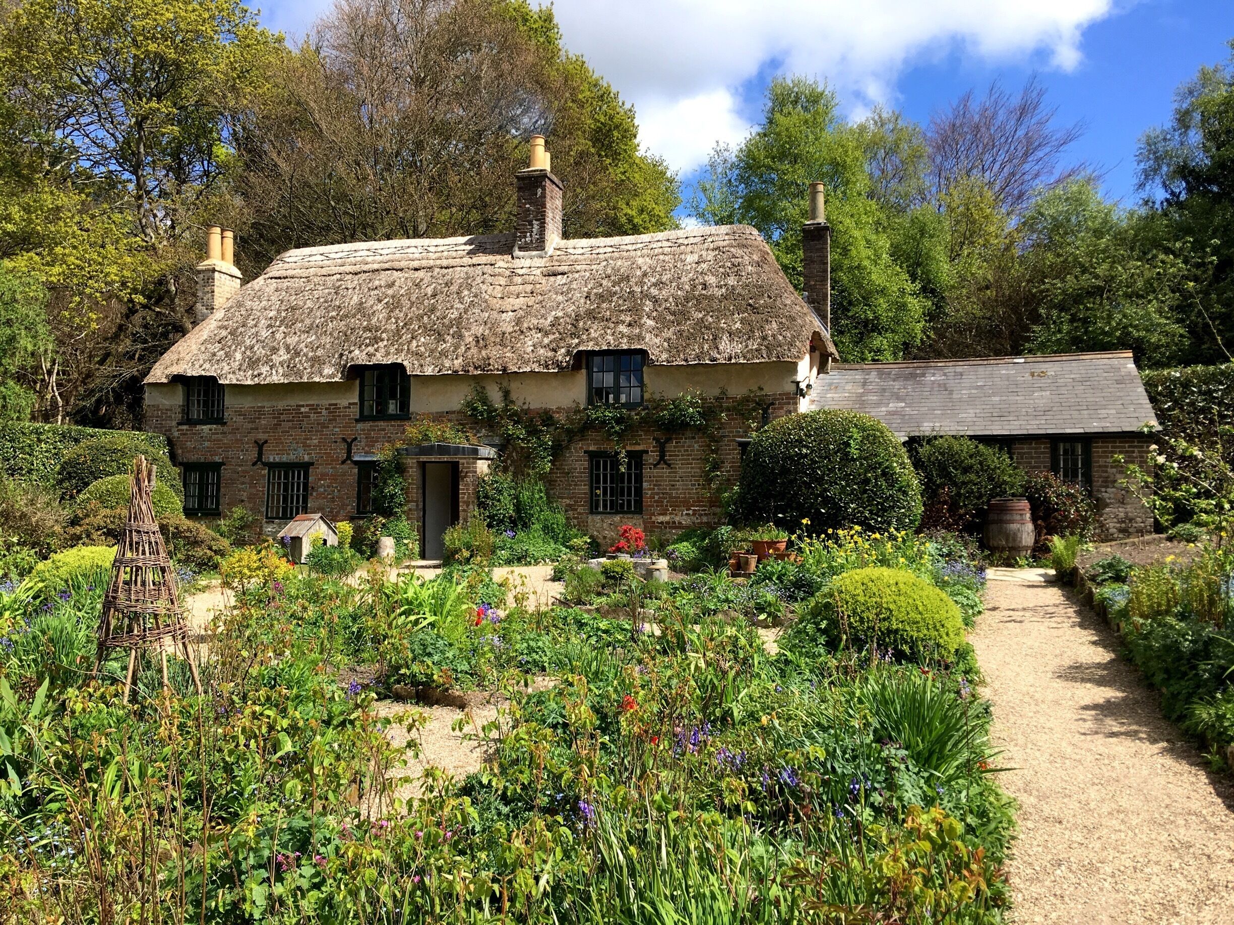 A thatched-roof house surrounded by a garden with various plants and flowers.