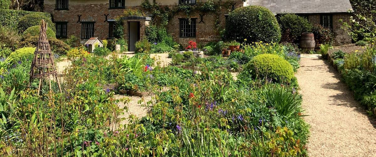A thatched-roof house surrounded by a garden with various plants and flowers.