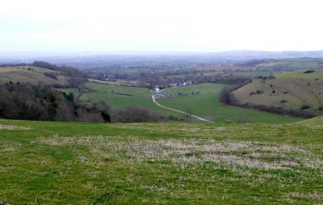 A valley with rolling hills, a winding road, and scattered buildings.