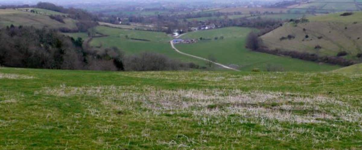 A valley with rolling hills, a winding road, and scattered buildings.