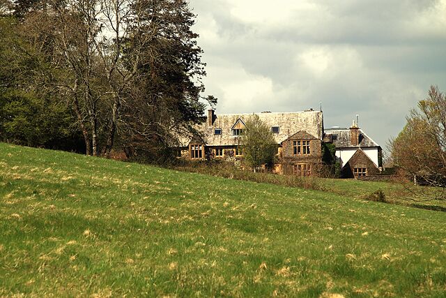 A stone house with multiple chimneys on a grassy hill.