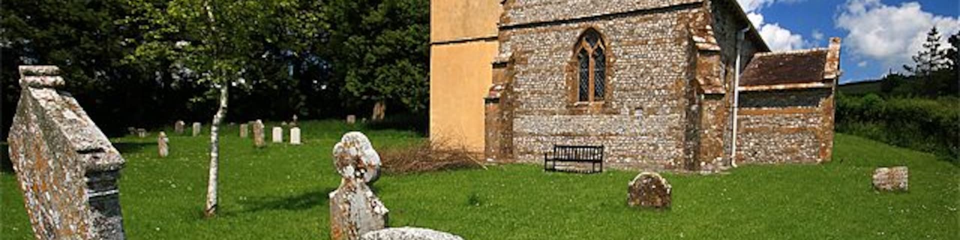 An old church with a stone facade, surrounded by a grassy cemetery with headstones.