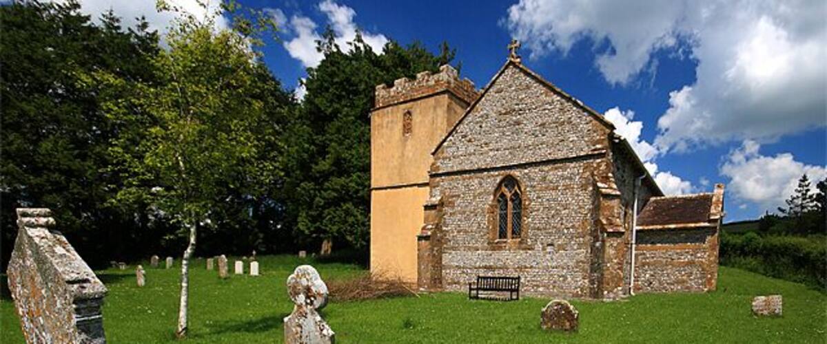 An old church with a stone facade, surrounded by a grassy cemetery with headstones.