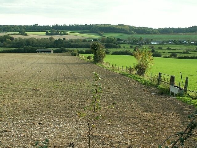 Un paisaje rural con un campo arado, una cerca y colinas ondulantes al fondo.