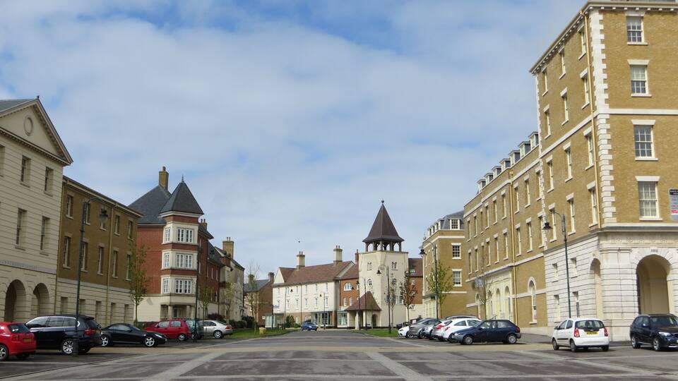 A street lined with historic buildings, parked cars, and a clear sky.
