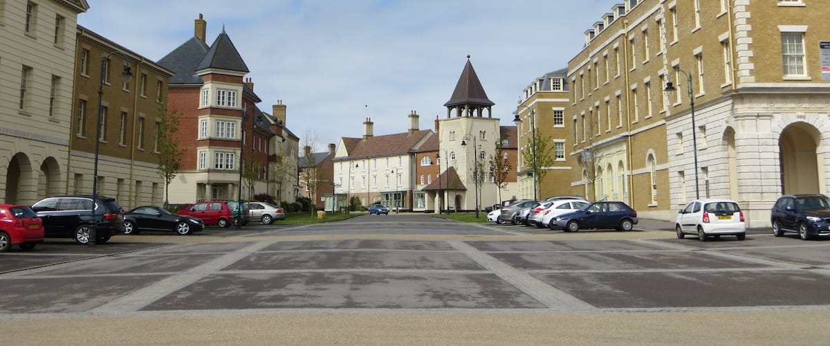 A street lined with historic buildings, parked cars, and a clear sky.