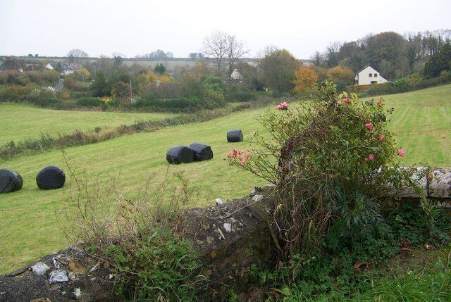 A rural landscape with hay bales, a stone wall, and a house in the background.