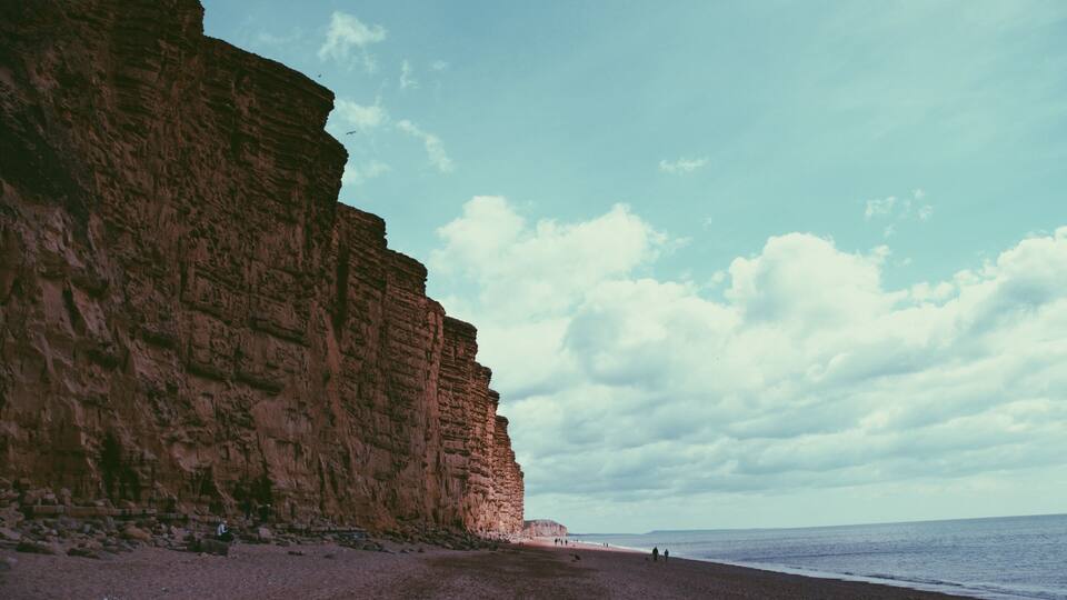 A beach with a large cliff and the ocean.