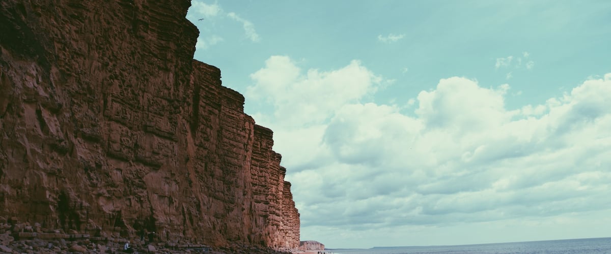A beach with a large cliff and the ocean.