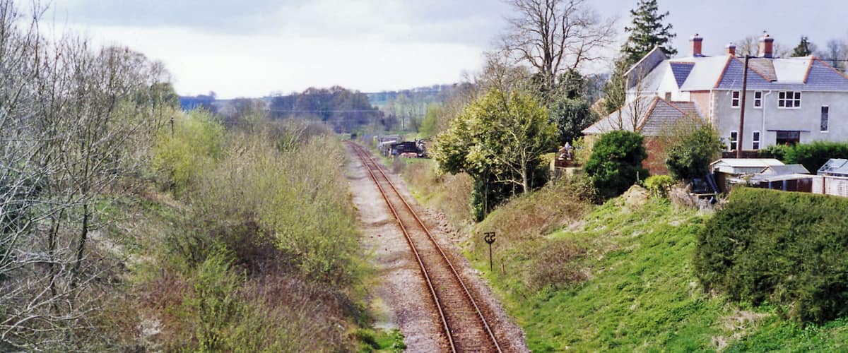 A railway track running through a rural area with houses on one side and trees on the other.