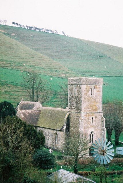 Una iglesia con un campanario y un molino de viento en un paisaje rural.