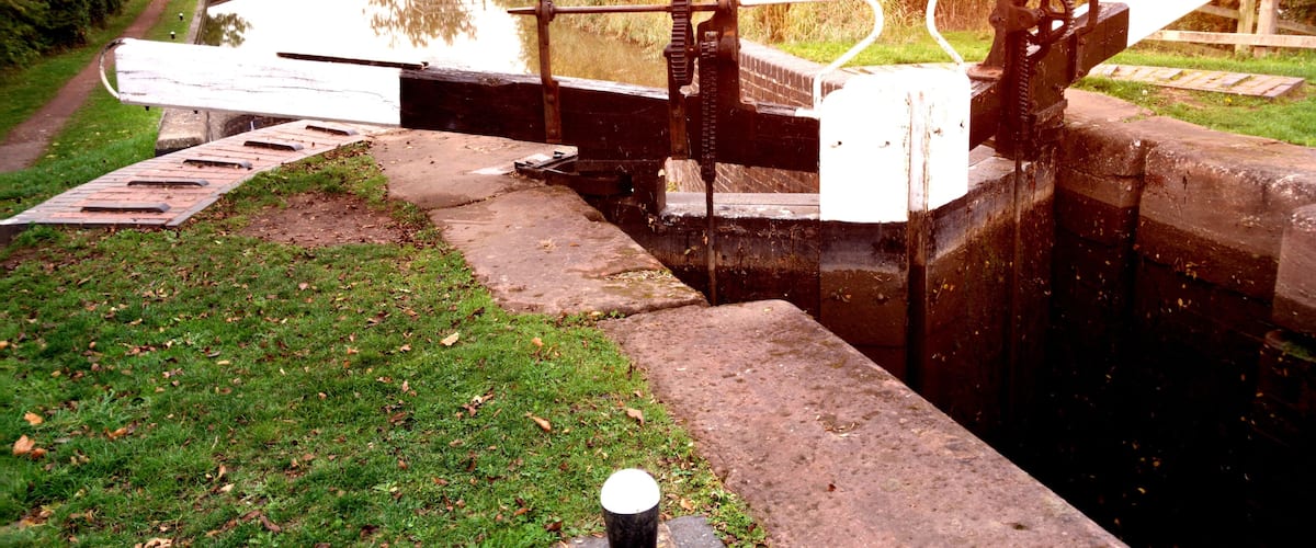 A lock gate on a canal with a grassy bank and trees in the background.