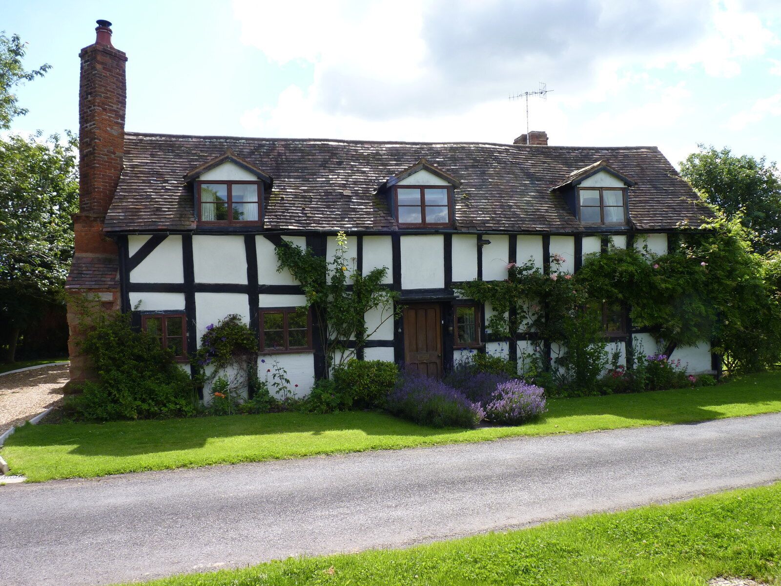 A traditional Tudor-style house with a steeply pitched roof, white and black timber framing, and a brick chimney.