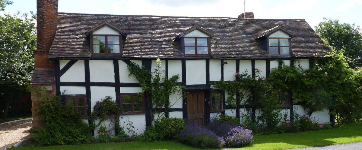 A traditional Tudor-style house with a steeply pitched roof, white and black timber framing, and a brick chimney.