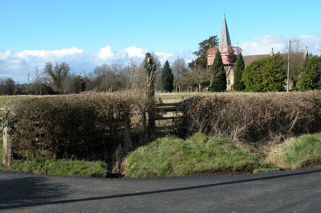 A rural road with a stone bridge, a church, and a field.