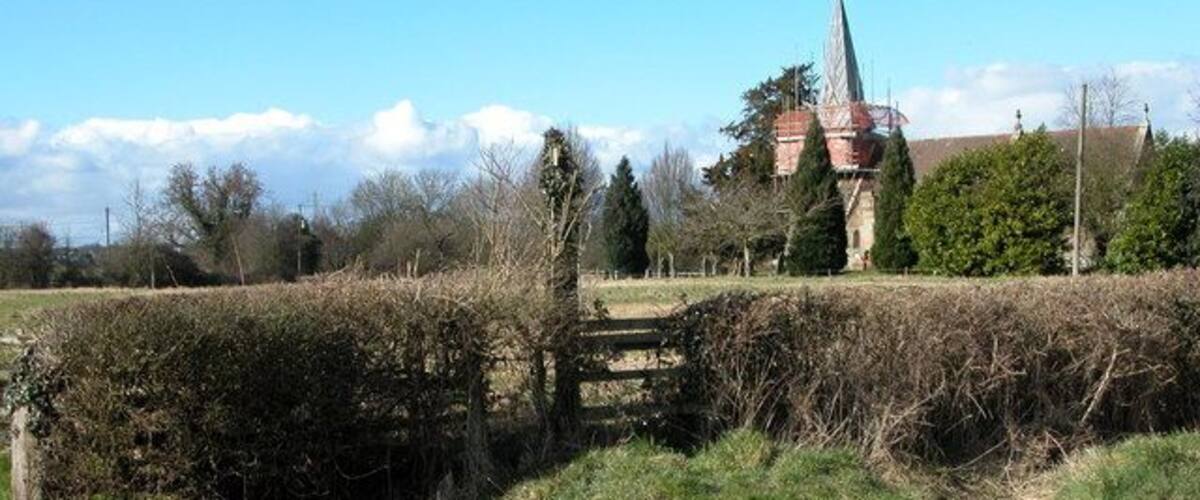 A rural road with a stone bridge, a church, and a field.