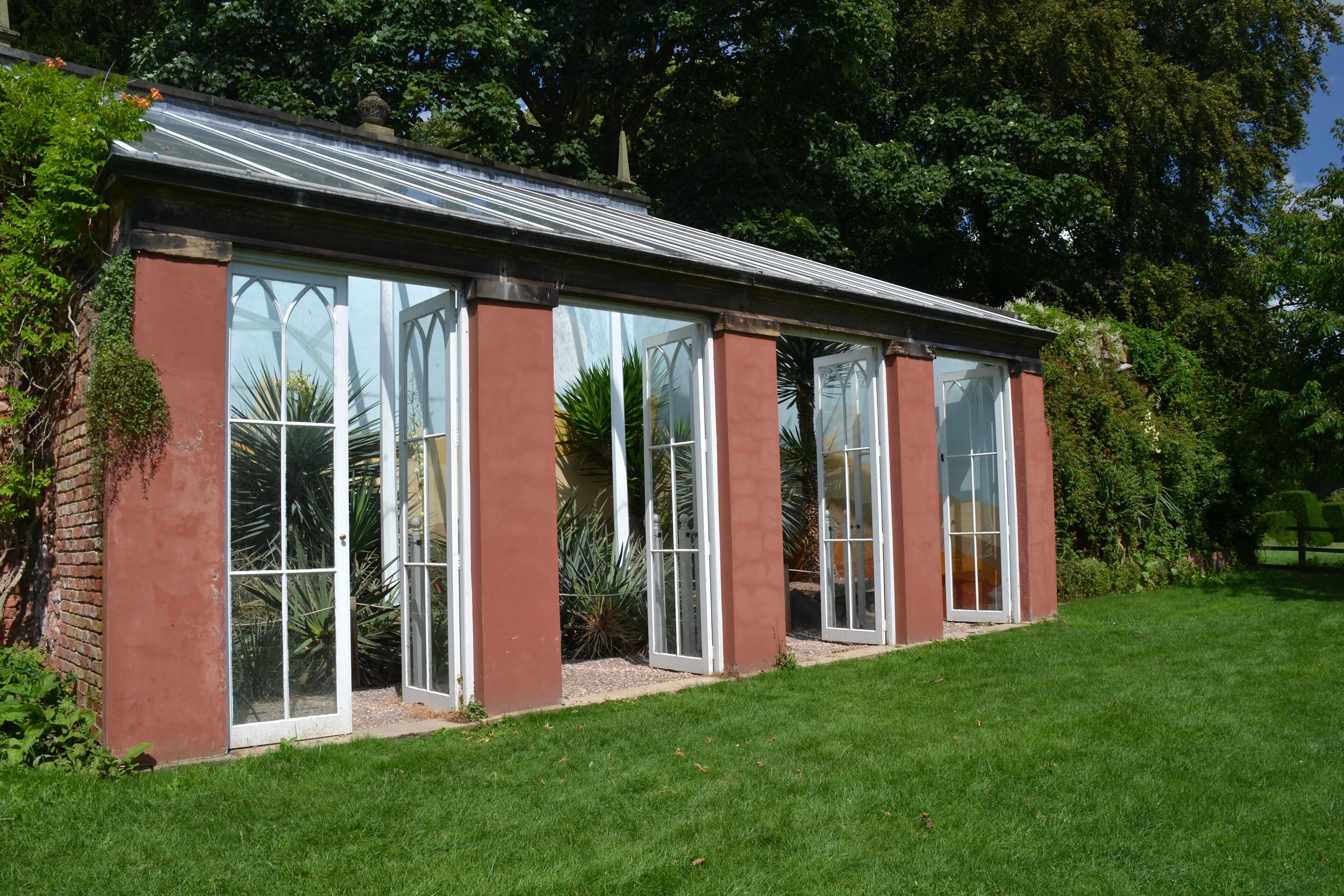 A conservatory with large glass doors, surrounded by a well-maintained lawn and various plants.