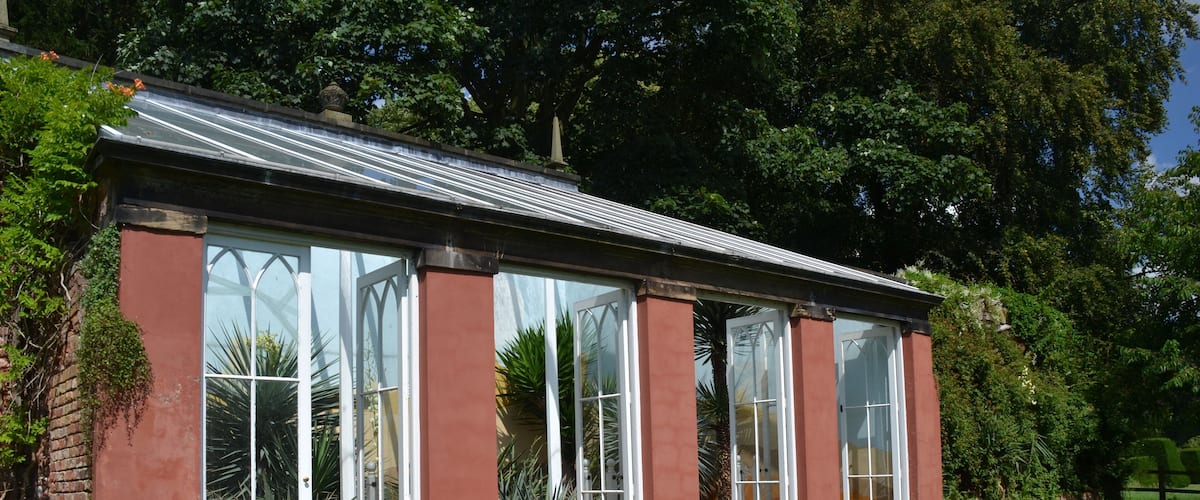 A conservatory with large glass doors, surrounded by a well-maintained lawn and various plants.