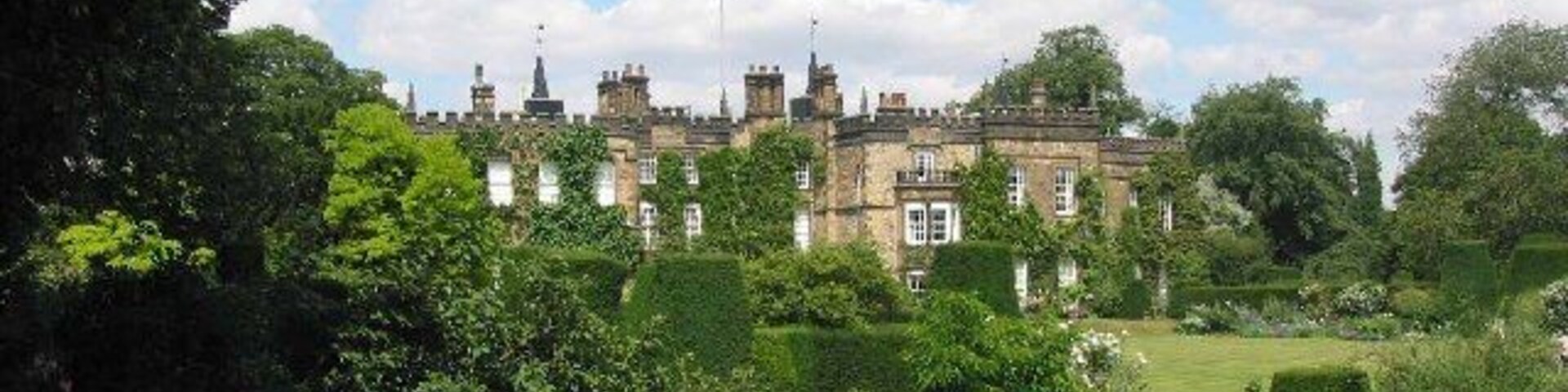 Um grande edifício histórico cercado por jardins exuberantes e árvores.
