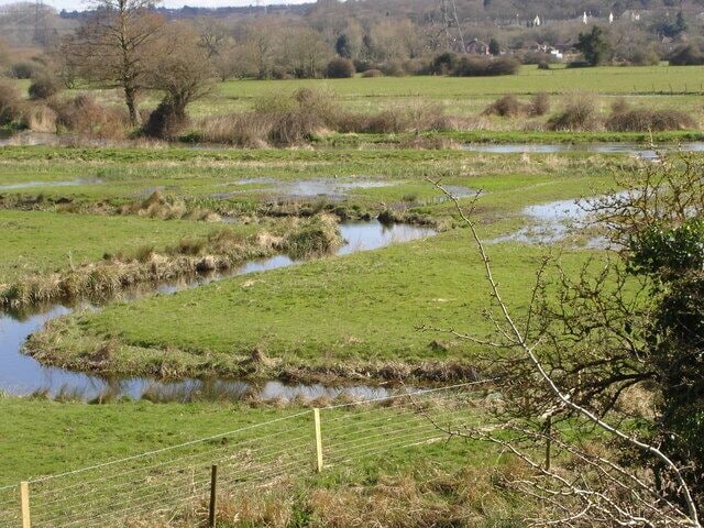 A rural landscape with a meandering stream, grassy fields, and a fence.