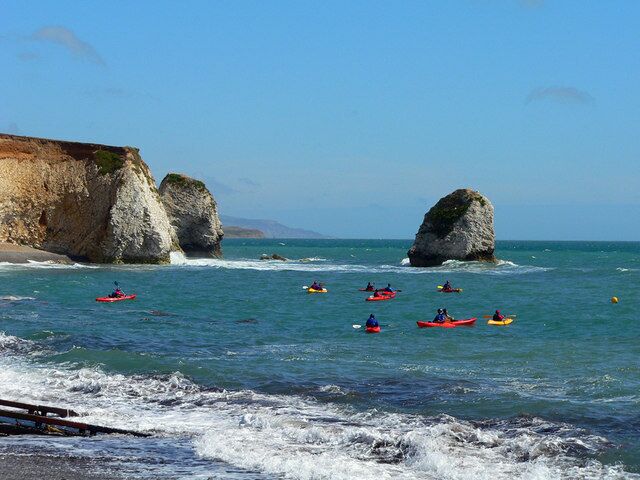 A coastal scene with kayakers on the water, cliffs, and large rock formations.